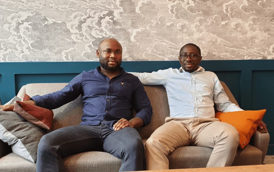 two people sitting on a sofa in business wear, smiling at the camera