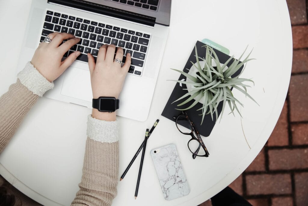 an above picture of a woman working on a laptop with a plant next to her